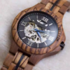 Black and gold transparent round skeletonized wooden men's automatic winding wooden watch with gold hands.