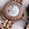 Black and gold transparent round skeletonized wooden men's automatic winding wooden watch with gold hands.